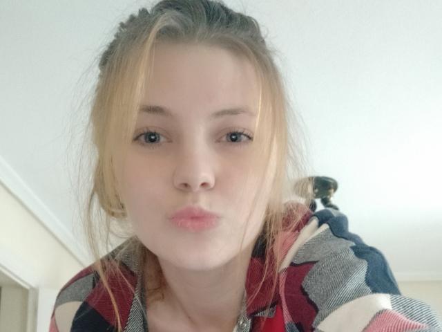 AdelaLoveX with puffy pink lips, blonde hair in messy bun, wearing red, black, and white plaid shirt, looking straight at camera with slightly parted pink lips.