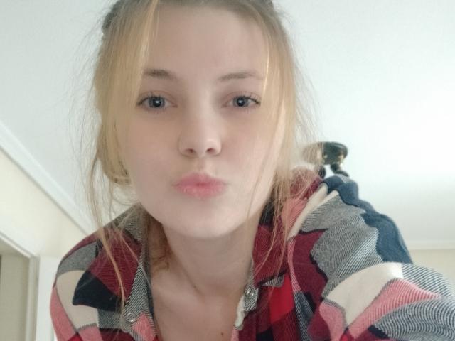 AdelaLoveX with pouty lips, blonde hair in a messy bun, wearing a red, black, and white plaid shirt, looking directly at the camera.