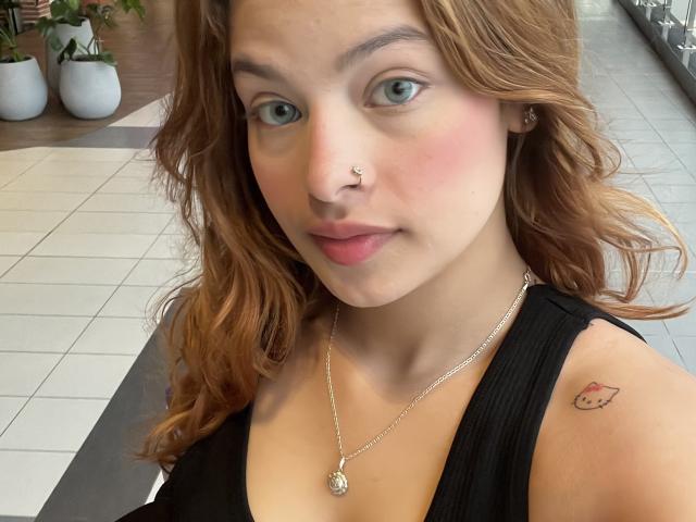 ShantalSummer has wavy brown hair, a nose ring, and a small Hello Kitty tattoo on her right shoulder. She's wearing a black top with a gold necklace.
