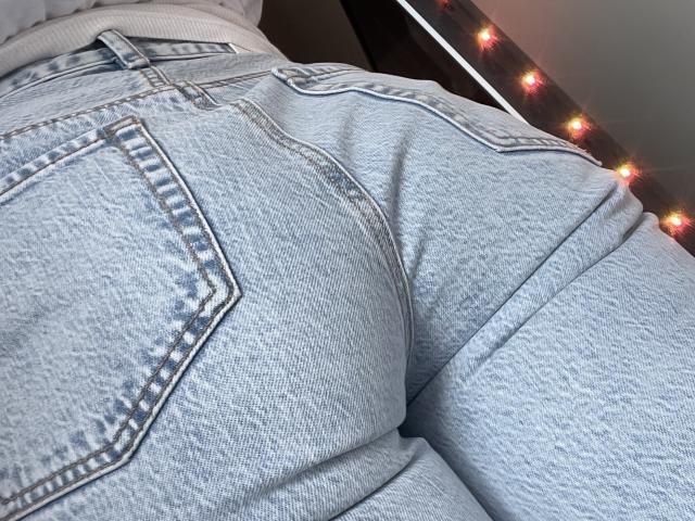 SandraSweet's butt in tight, light-blue denim jeans with visible pockets, slightly textured fabric, and white stitching. String lights in background. Close-up, bottom-up perspective.