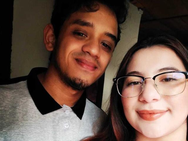 KayDwayne with curly brown hair and beard, wearing a gray and black polo, smiles next to KayDwayne with glasses, brown hair, and pink lipstick.