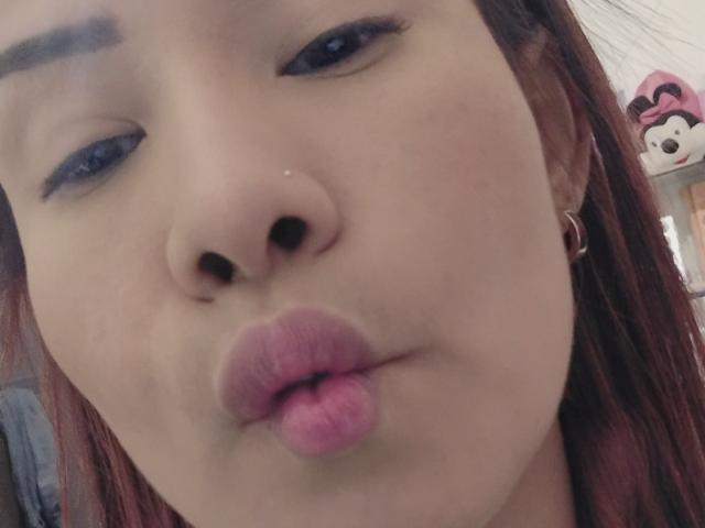 Les lèvres roses et légèrement retroussées de NathashaRomexo font une grimace amusante, avec son nez légèrement relevé et un trait d'eye-liner bleu foncé. Elle a les cheveux roux et un petit piercing au nez..