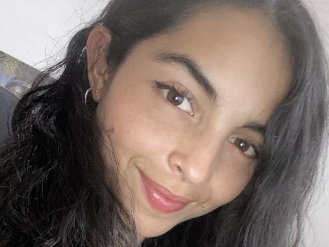AngelineS ha la pelle marrone media, i capelli scuri e ondulati, gli occhi marroni, un piccolo orecchino a cerchio, un leggero sorriso e labbra rosse rosate. Il suo viso è centrato e guarda leggermente a destra..