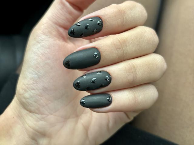 Pingli's hand with matte black nails, each adorned with small shiny star-shaped stickers, showing off her stylish and edgy nail art.
