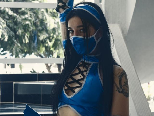 DulceHarper with long black hair, blue mask, matching gloves, and a revealing blue top with black criss-crosses. Tattoo on right arm. Holding a blue book. Sultry, confident look.