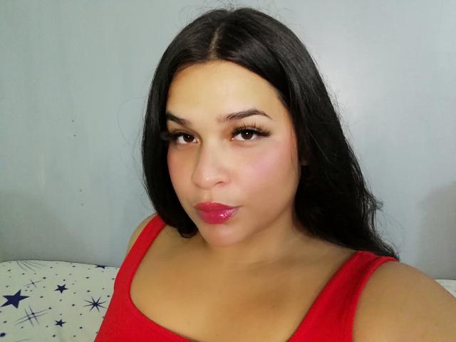 AntonelaPark with long black hair, wearing a red tank top, has pouty pink lips, dark eyelashes, and a cute, slightly chubby face. Boobs visible under the top.