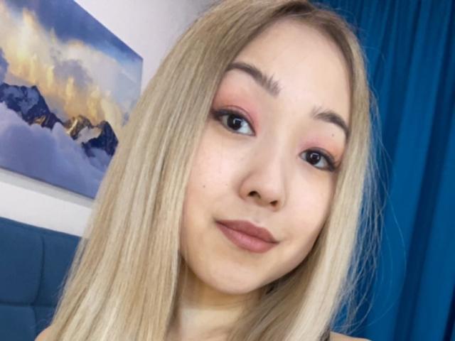 RenyLime has blonde hair, pink eyeshadow, and pink lipstick, with a slight smile, looking at the camera, showing her cute face and small nose.