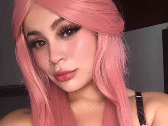 ShantallParis with pink hair, nose ring, and pink lipstick, has long eyelashes, pink blush, and a cute tattoo on her shoulder, wearing a black strap top.