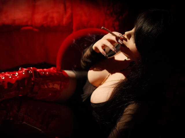 GabrielaAroms with large boobs, black hair, red lace-up boots, black top, sucking on a cigarette, dark shadowy background, red light, leaning back, sexy, seductive, dark ambiance.