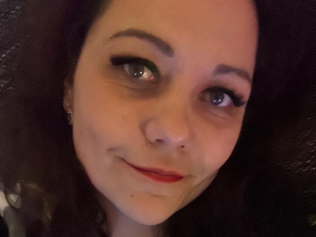 DoriSexis ha la pelle chiara, i capelli ricci e scuri, gli occhi verdi con lunghe ciglia, un piccolo piercing al naso e un leggero sorriso con rossetto rosso. La foto è leggermente sfocata..