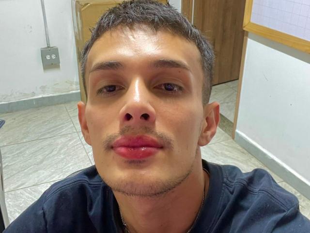 SlimLewis has a cute face with short dark hair, a small mustache, and shiny pink lips. He's wearing a black shirt, and there's a gold necklace.