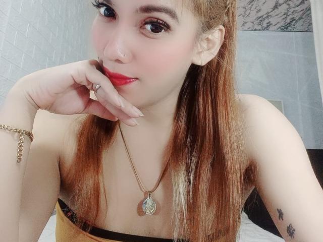SeductiveAngelX has red lipstick, straight brown hair, a gold necklace, and is touching her glossy red lips with her finger. She has a nose ring and a tattoo.