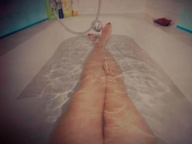 BlackBerryAmelia's legs are in a white bathtub, water is clear, showing her pale skin with red toenails. She's lying down, feet crossed at the ankles.