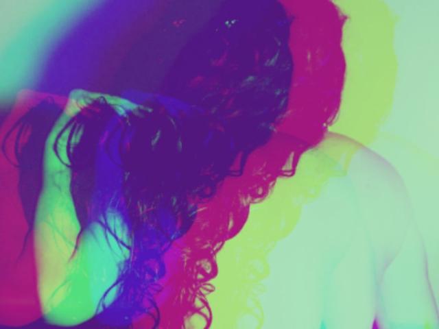 A colorful, abstract shot of MilfRosaly's curly dark hair, back and shoulders, with neon green, pink, blue, and yellow light effects, highlighting her bare, pale skin.