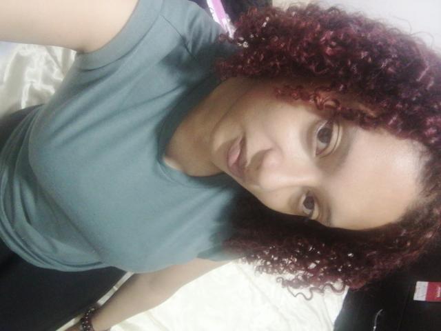 VioletaSwitch with curly red hair, wearing a green tee, has a small nose and is looking at the camera with a slight pout. Her tits are not visible.