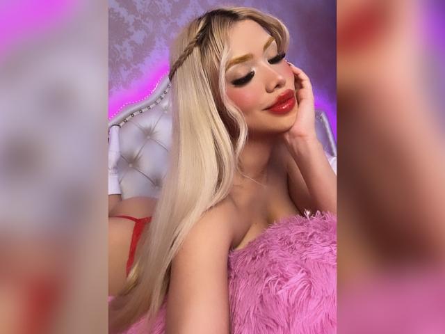 ChristieGarci with long blonde hair, braided crown, pink fluffy dress, red lipstick, hand on cheek, eyes closed, pink and purple lighting, white tufted headboard, visible red thong butt.
