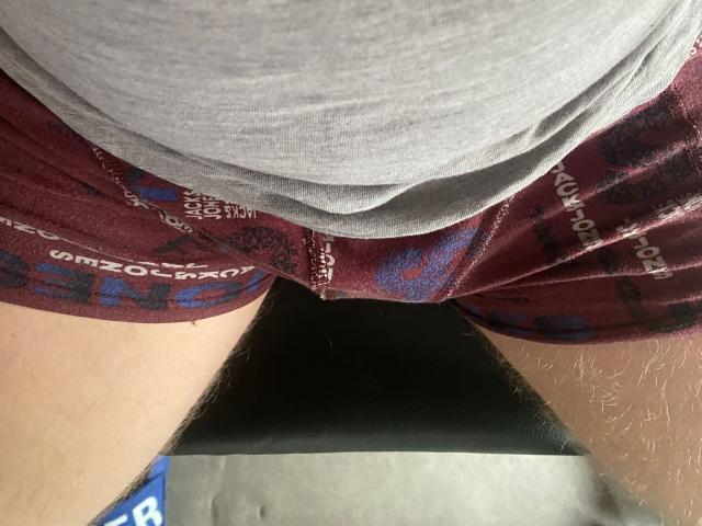 Koentje trägt eine marineblaue Boxershorts, die leicht heruntergezogen ist, mit sichtbarem schwarzen Schamhaar und ein graues Hemd darüber. Konzentrieren Sie sich auf den unteren Rücken und die Gesäßpartie..