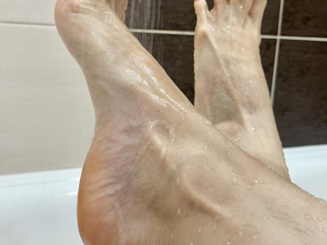 TheHottestBlonde's soles are up in the shower, water droplets running down their pale, slightly pinkish feet. The toes are spread, showing the smooth, wet skin.