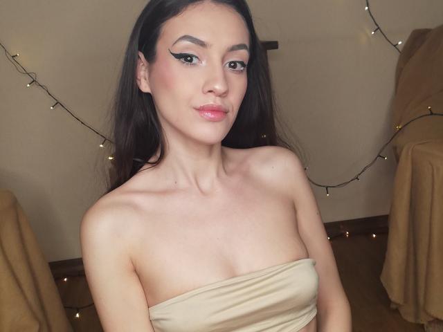 Vievienne Clemente, con cabello largo y oscuro, vestida con un top beige sin tirantes que deja ver sus senos, labios rosados y brillantes, delineador de ojos, mirando a la cámara con una ligera sonrisa..