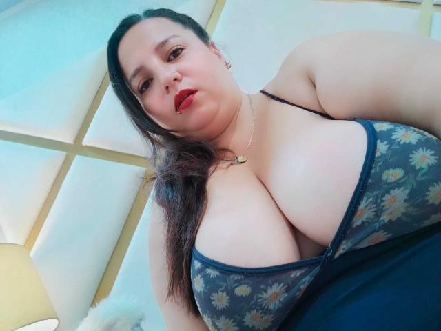 SkayLaraWalker has big, fluffy tits in a floral-patterned bra, red lipstick, and long dark hair, wearing a necklace, looking down at the camera.