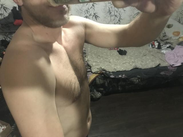 ArthurXMen est un homme torse nu, avec une poitrine poilue, et il prend un selfie devant un miroir, montrant sa partie supérieure du corps et un tatouage sur son bras droit..