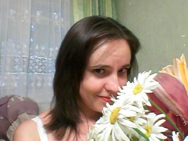 MelanieAhHot with brown hair, white lace top, holding daisy bouquet, smiling slightly, cute face, soft light, casual setting, subtle makeup, relaxed vibe, boop-boop.