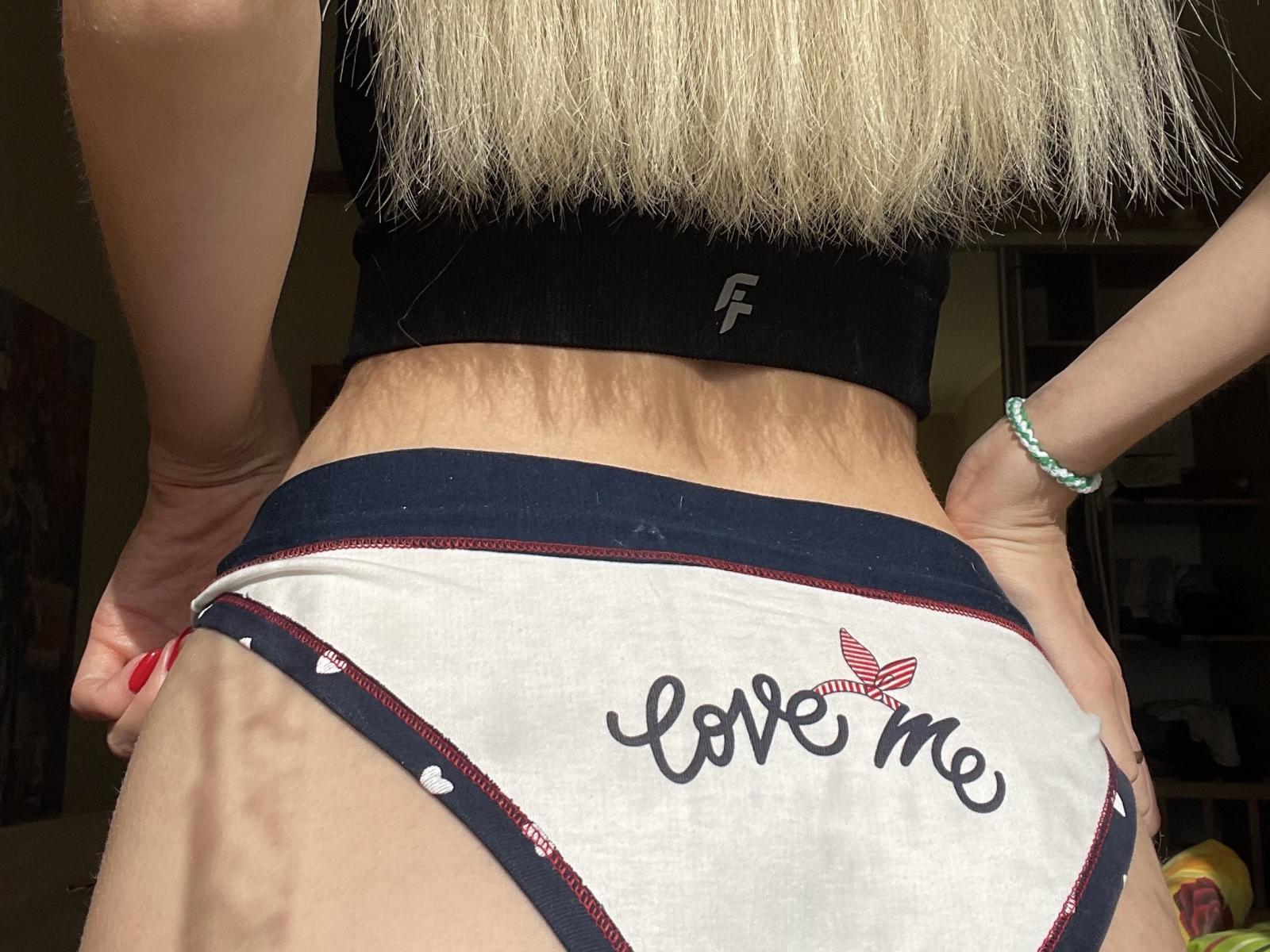 MagicalIceone's pale butt in white panties with "Love Me" and a red heart, black top, blonde hair, and green bracelet, hands on hips, red nails.