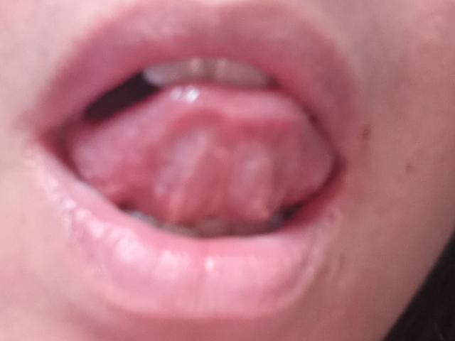 LaFrancaiseJessy's pink tongue is sticking out of her slightly parted pink lips, showing her teeth. The image is a close-up of her mouth and tongue.
