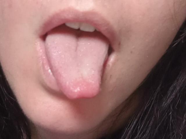 LaFrancaiseJessys Mund ist geöffnet, ihre rosa Zunge steckt heraus, wodurch ihre weißen Zähne und leicht geöffnete, rosa Lippen sichtbar sind. Ihre helle Haut ist zu sehen..