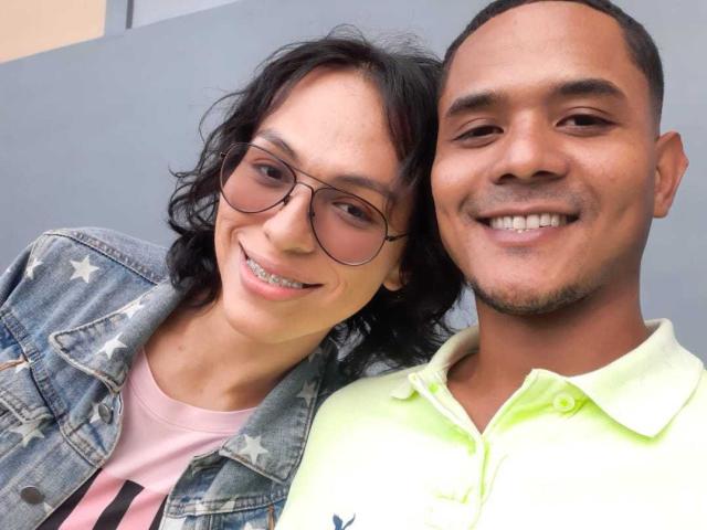 AdrianaYMaicol69 with wavy black hair and glasses, smiling, wearing a star-studded denim jacket. Maicol69, with short black hair and beard, smiling in a neon green polo.