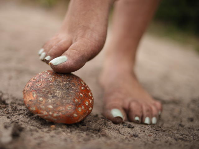 Il piede di AbbySton, con le unghie dipinte di bianco, è appoggiato su una roccia arancione sporca e maculata, su una superficie sabbiosa..