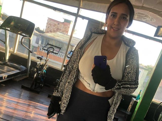 BlueWaters with medium tits, wearing a zebra-patterned jacket, white sports bra, and black high-waisted pants, holding a purple phone, smiling in a gym.