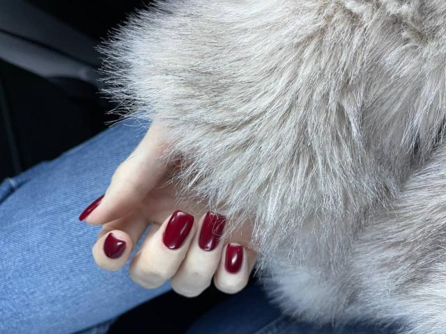 La mano de Zuckerberg, con uñas rojas brillantes, descansando sobre una pierna de mezclilla azul, cubierta por un puño de piel sintética gris esponjosa. Los senos no son visibles, el enfoque está en las uñas y la piel..
