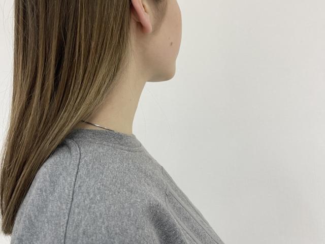 MiaMoone's side profile showing her brown, straight hair, gray shirt, and small dark mole on her left cheek. Her ear is visible, and she's facing right.