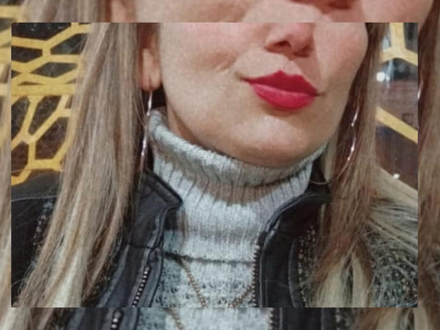 GiuliaAddams with pouty red lips, wearing a gray turtleneck and black leather jacket, hoop earrings, and blonde hair, slightly visible nose and chin.