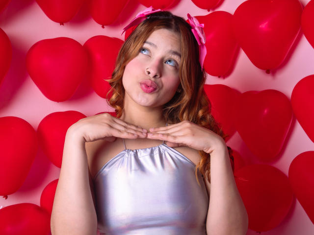 ShantalSummer with pouty pink lips, wearing a silver satin top, pink hair bow, hands near neck, red heart balloons in background, light skin, blue eyes, slightly chubby.