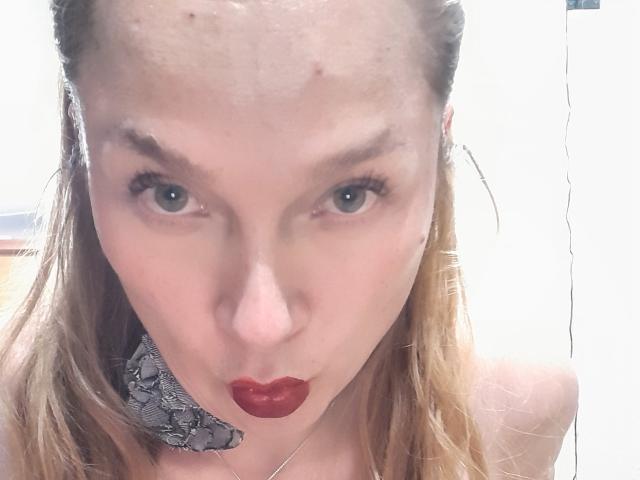 Metztona, con rossetto rosso, labbra piene e un copricapo con motivo a serpente, ha una fronte lucida, occhi azzurri e lunghi capelli biondi, e guarda direttamente verso la telecamera..