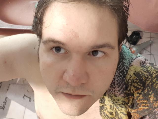 NectarineFad has a pale face, short brown hair, blue eyes, and a slight beard. He's shirtless with a towel on his right shoulder, looking up at the camera.
