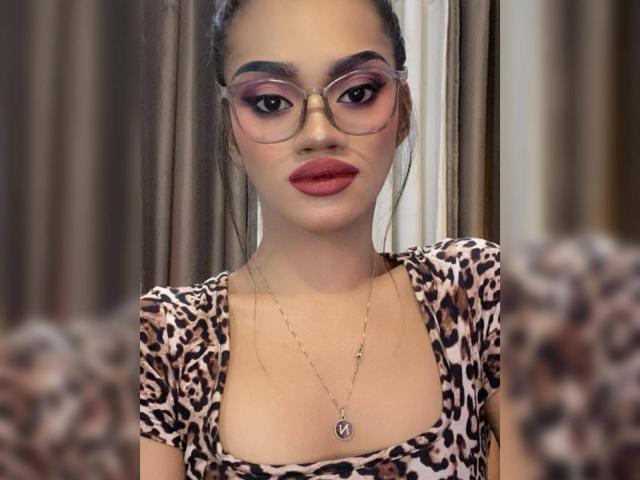 SevenInchesCockTS heeft roze brillen, roze oogschaduw, rode lippenstift en een top met luipaardprint. Ze draagt een ketting met een "V"-bedel. Haar borsten zijn klein en schattig..