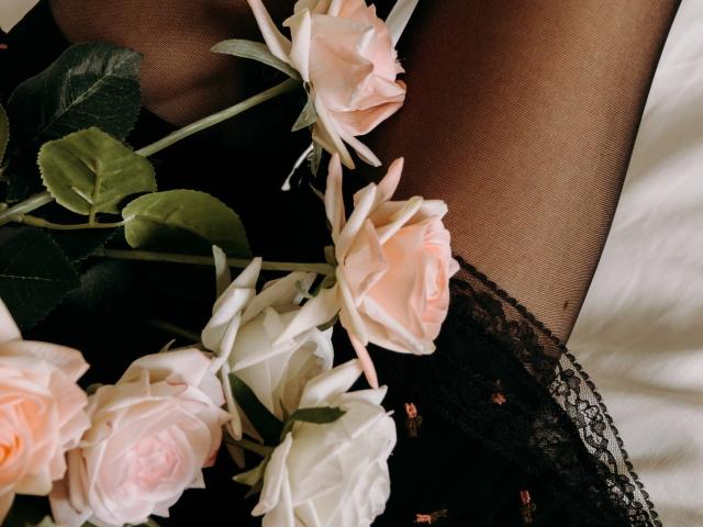 TinaRedly's leg in black sheer stockings, with a bouquet of pink and white roses, green leaves, and black lace, resting on a white surface.