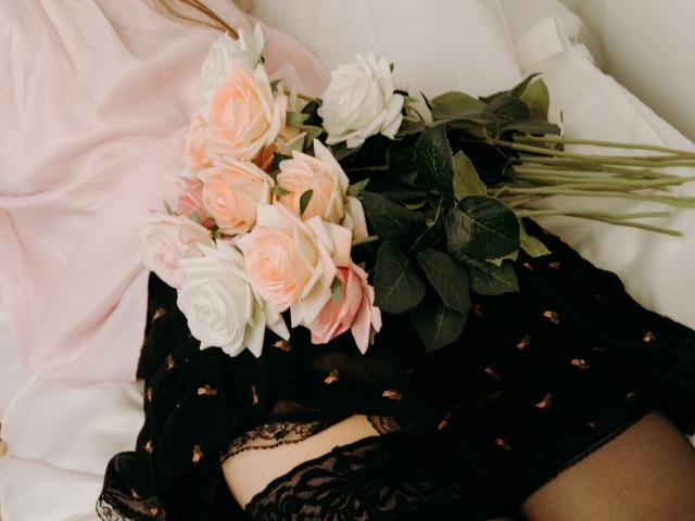Tinas schwarze Spitzenunterwäsche und der schwarze Rock mit rosa Rosenmustern, zusammen mit einem Strauß aus weißen und rosa Rosen, schwarzen Spitzenstrümpfen, einem rosa Hemd und weißen Kissen..