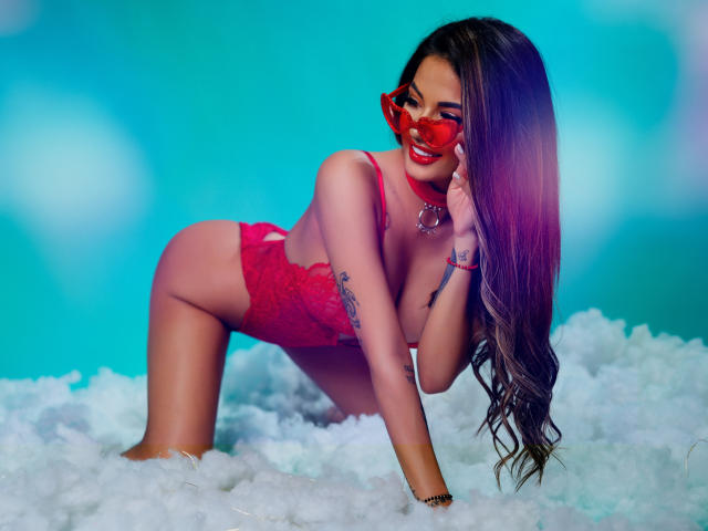 Yuukenzi with red lingerie, red sunglasses, and long brown hair, on all fours in fluffy white stuff, showing her ass and tits, smiling, tattoo on her left arm.