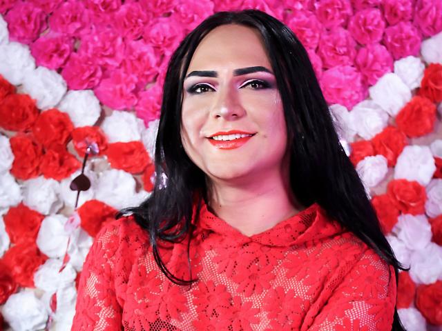 Iris Durand, avec de longs cheveux noirs, un haut en dentelle rouge, un fond de roses roses et blanches, souriante, rouge à lèvres rouge, fard à paupières violet, poitrine moyenne, peau claire, sourcils foncés, mignonne..