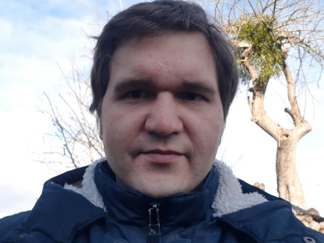 NectarineFad has a chubby face with short brown hair, a slight mustache, and is wearing a blue jacket with white fur. His nose is slightly red.