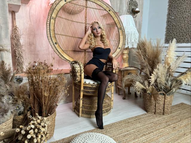KatarinaPretty with blonde curls, black strapless top, black shorts, and black stockings, sitting in a wicker chair, showing her tits and ass, with puffy reed decor.