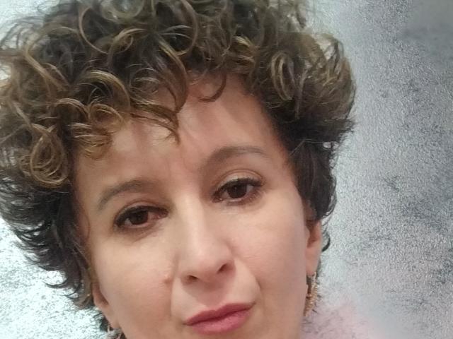 NikHotty has curly brown hair, light skin, brown eyes, and a slight smile. She's looking at the camera with a relaxed expression. Her pink lipstick stands out.