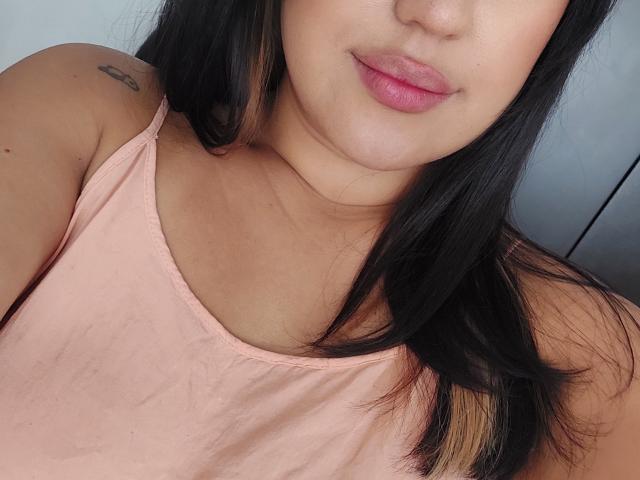 LauraRichis with pink lips, black hair, light skin, small tattoo on left shoulder, wearing pink tank top, showing a little bit of her tits.