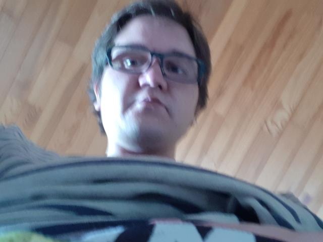 NectarineFad, wearing glasses, with a slightly upturned nose, staring down, blurry lower face, and brown curly hair, in a wooden ceiling photo, looking serious.