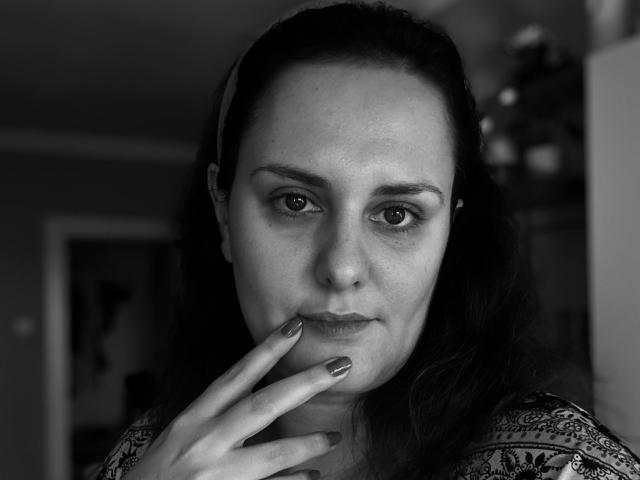Black-and-white photo of CurvySweetGirl with dark hair in a headband, hand touching her chin, looking at camera, wearing a patterned shirt, nails painted metallic.