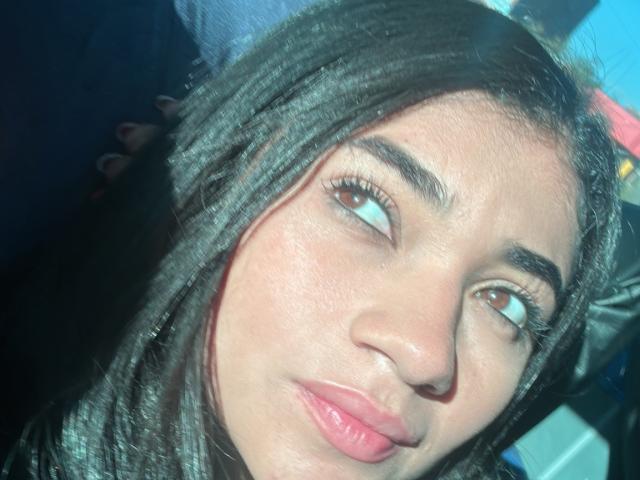 AmberSkylerr has dark brown hair, brown eyes, and pink lips. Her face is slightly squished with a pouty expression, showing her nose and smooth skin.
